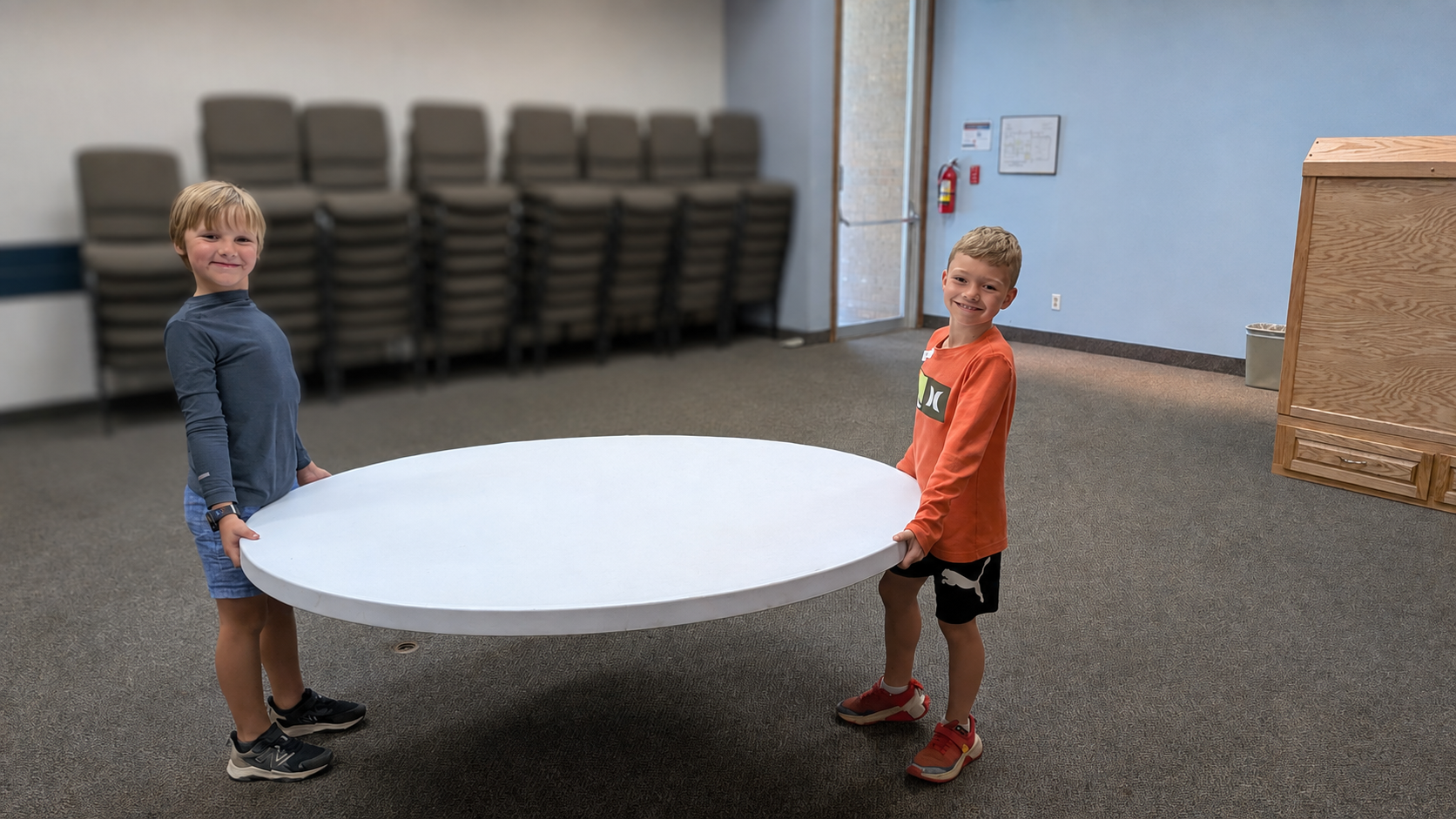 Two Fontes children carrying a table as the community prepares its new learning space